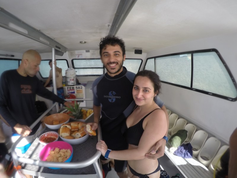 A couple with scuba diving gear on a boat eating refreshments
